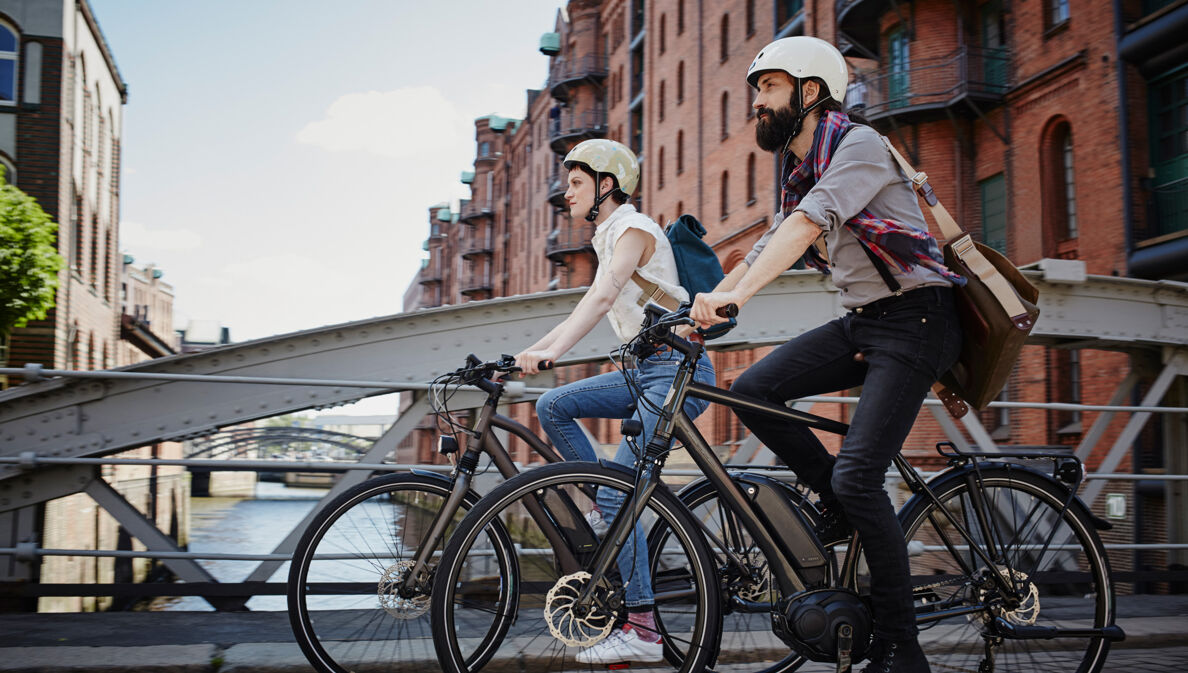 Ein Mann und eine Frau mit Fahrradhelmen fahren auf E-Bikes durch die Hamburger Speicherstadt.