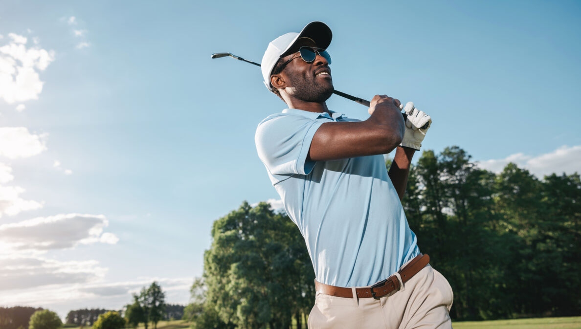 Porträt eines dunkelhäutigen Golfers in einem blauen Poloshirt beim Abschlag auf einem Golfplatz