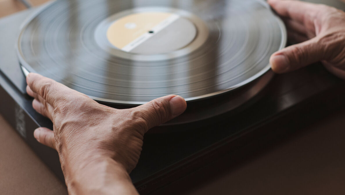 Zwei Hände, die das Vinyl auf dem Plattenteller aufnehmen