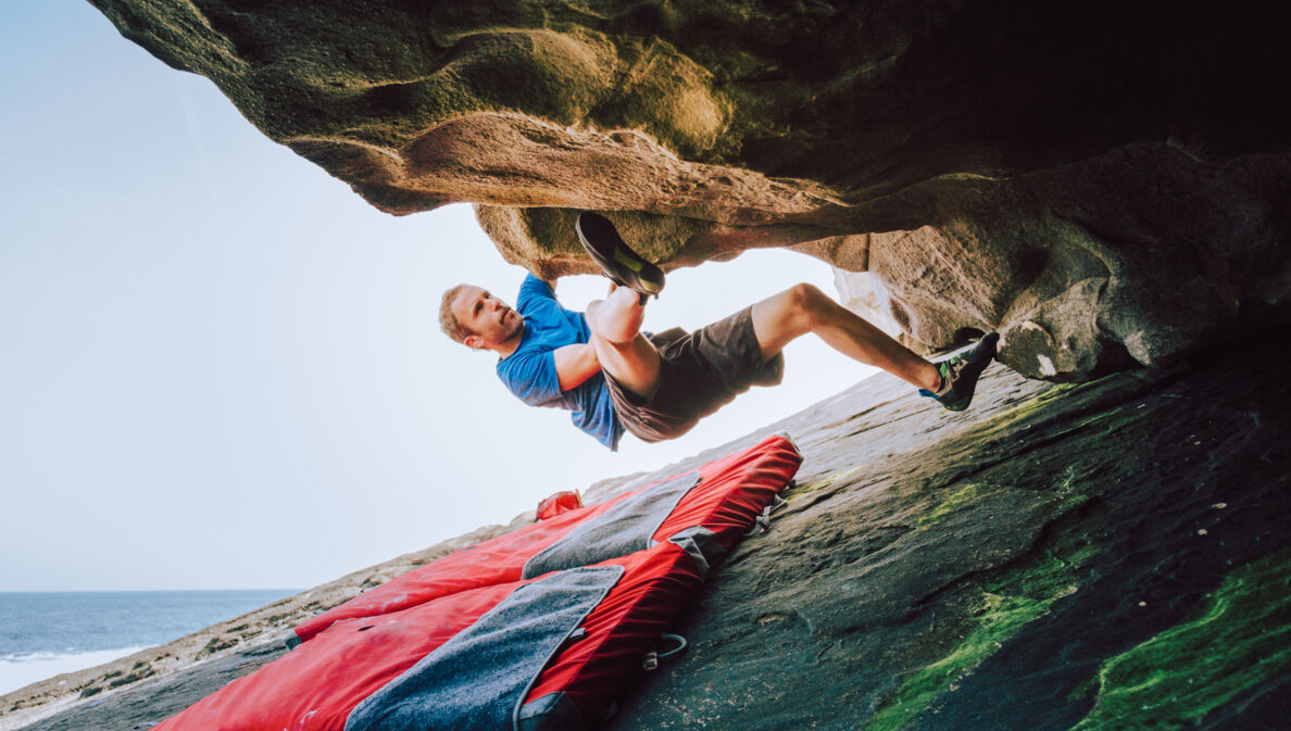 Ein Mann bouldert am Felsen, unter ihm liegt eine Matte