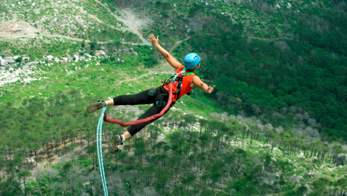 Eine Frau springt von einer Klippe am Bungeeseil in den Abgrund.