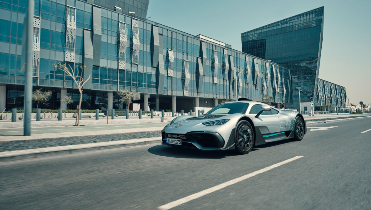 Silbernes Rennauto auf der Straße vor einem gläsernen Haus.