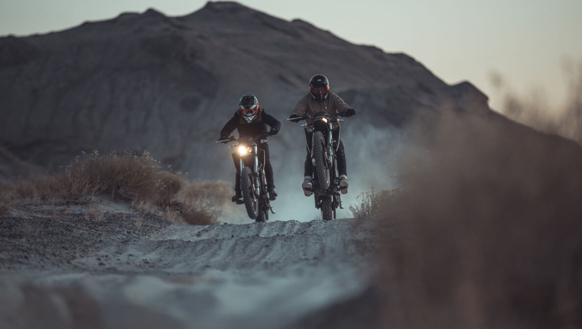 Zwei Motorradfahrer fahren in der Dämmerung durch eine Wüstenlandschaft