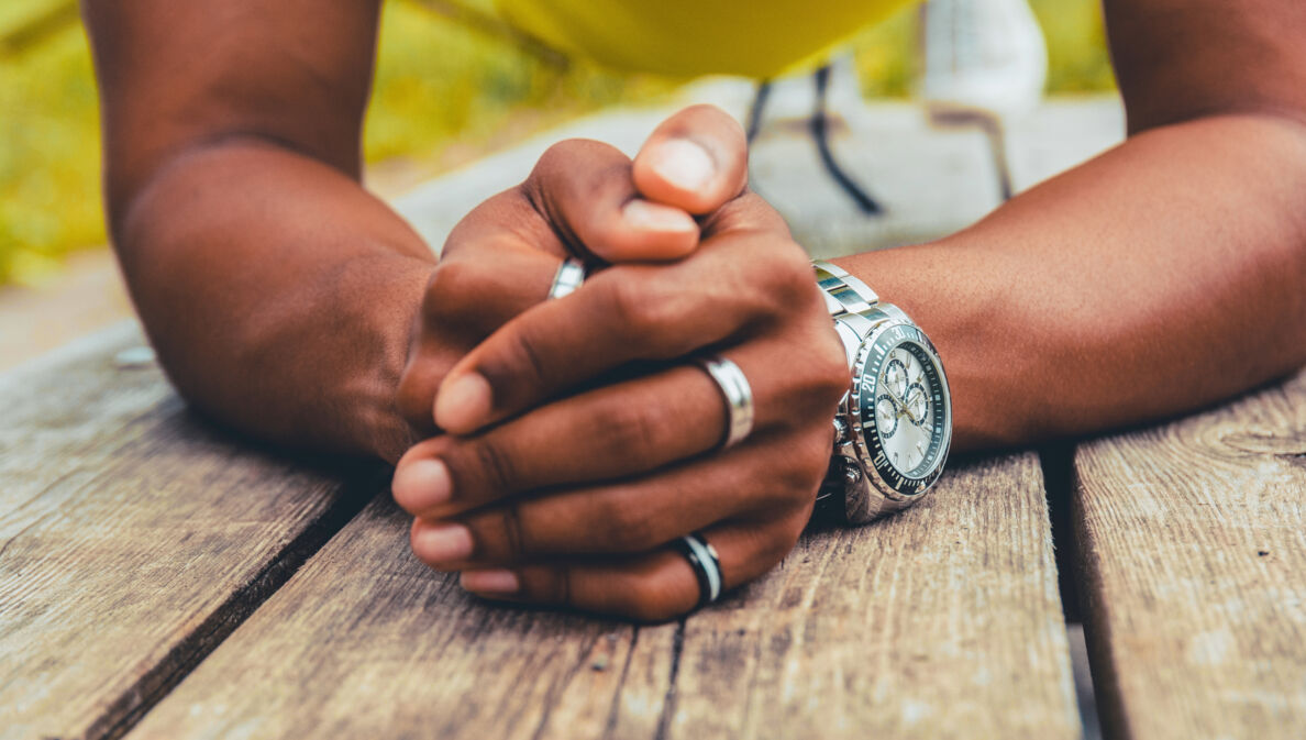 Gefaltete Männerhände mit silbernen Ringen und einer Uhr am Handgelenk