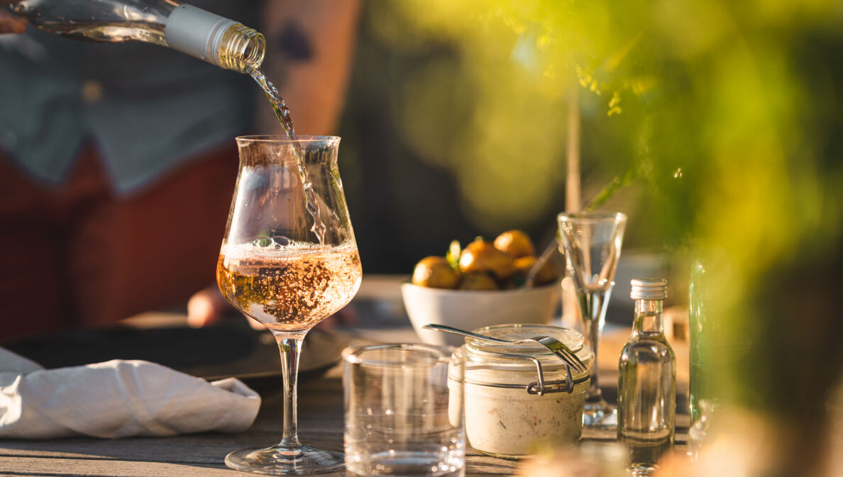 Ein Glas auf einem gedeckten Gartentisch, in das Rosé eingeschenkt wird