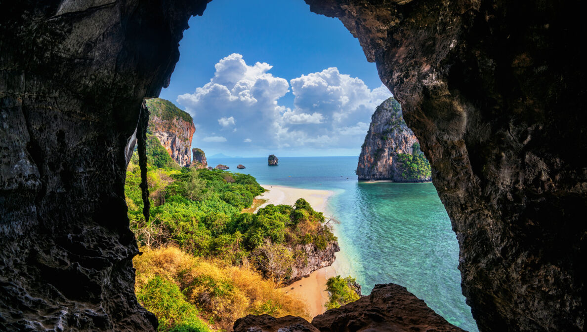 Blick aus einer Höhle auf Strand, Meer und Bäume