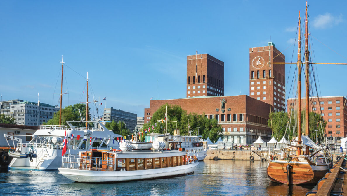 Blick auf das rote Rathaus von Oslo mit Backsteintürmen vom Wasser aus, im Vordergrund Segelboote