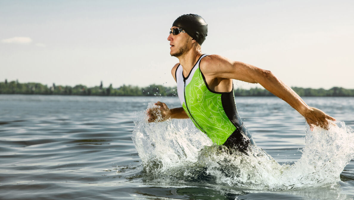 Ein durchtrainierter Triathlet mit Badekappe und Schwimmbrille rennt ins Wasser