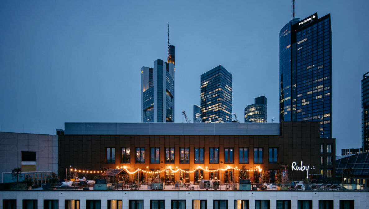 Eine beleuchtete Rooftop-Bar vor der Frankfurter Skyline bei Nacht