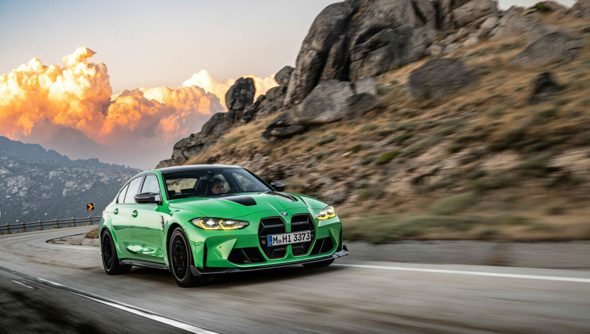 Ein grüner BMW auf einer Landstraße, im Hintergrund große Wolken und Berge