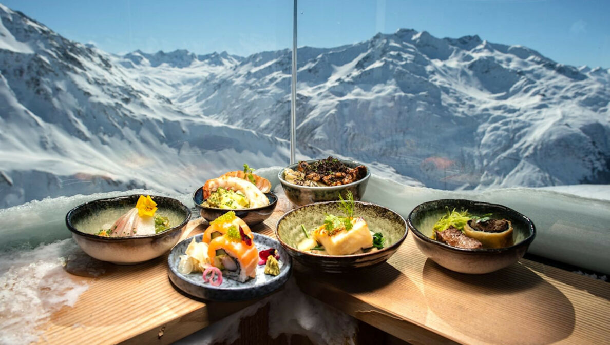 Japanisch angerichtete Teller auf einem Holztresen, im Hintergrund das Panorama von Andermatt