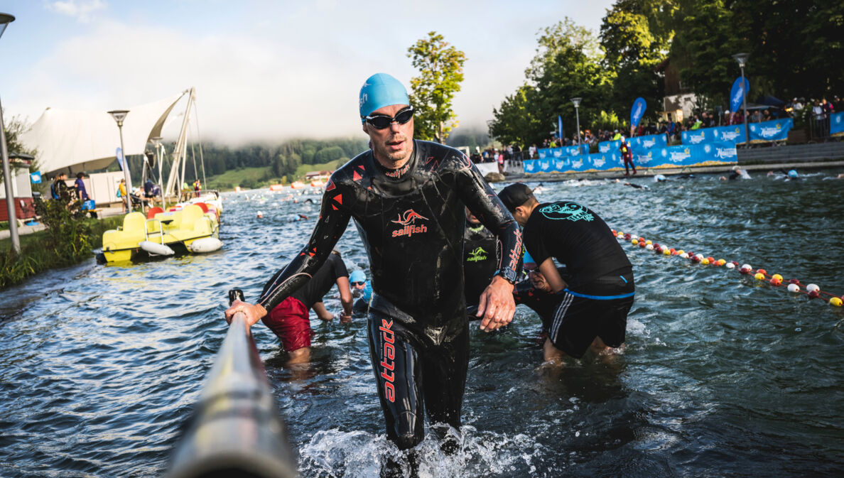 Eine Person im Neoprenanzug steigt aus einer Wasserquelle heraus