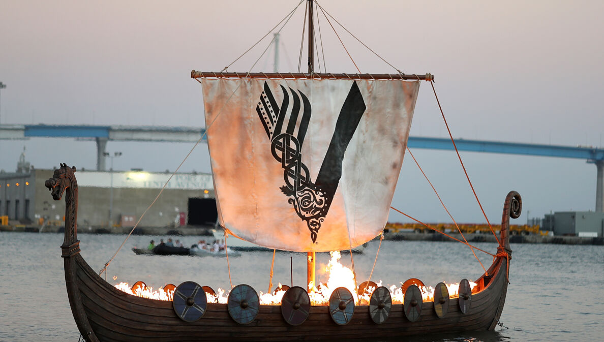 Aufnahme eines brennenden Wikingerschiffs auf dem Meer mit einem Segel, das das Logo der „Vikings“-Serie zeigt