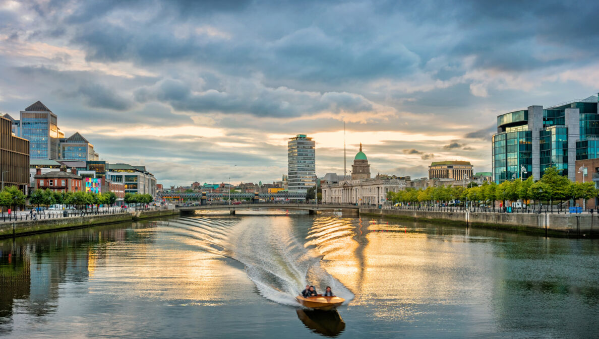 Ein Motorboot fährt auf dem Liffey River in Dublin bei Sonnenuntergang