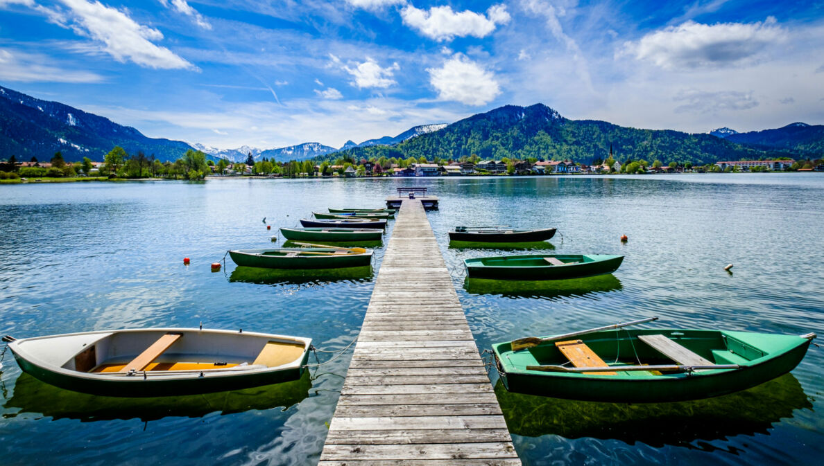 Ein Holzsteg mit kleinen Booten auf einem See, im Hintergrund Berge