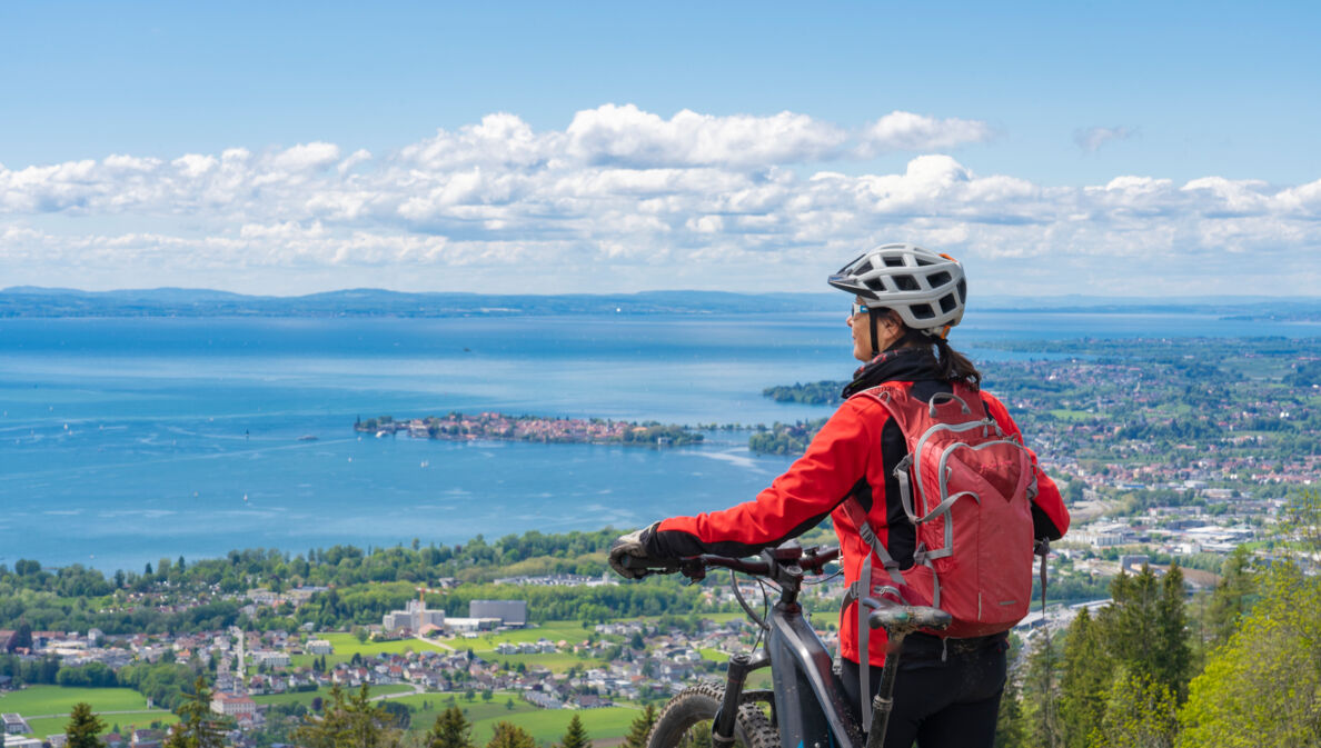 Rückansicht einer Frau mit einem Fahrrad vor dem Panorama des Bodensees