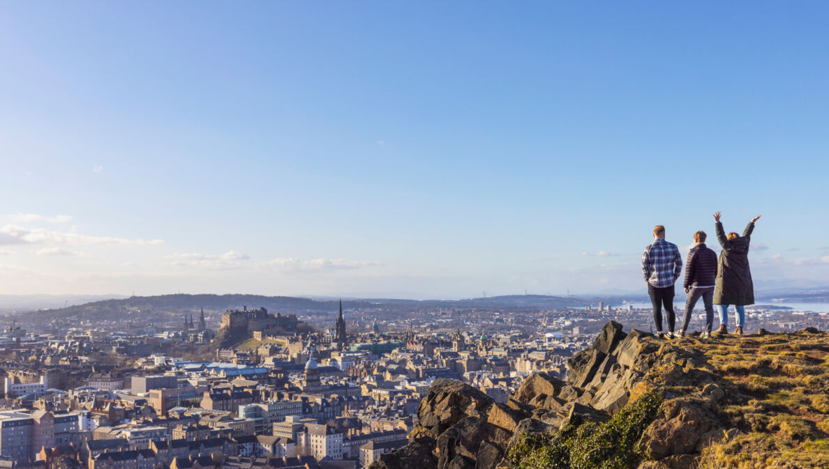 Drei Personen stehen auf einer Erhöhung und blicken von dort über Edinburgh