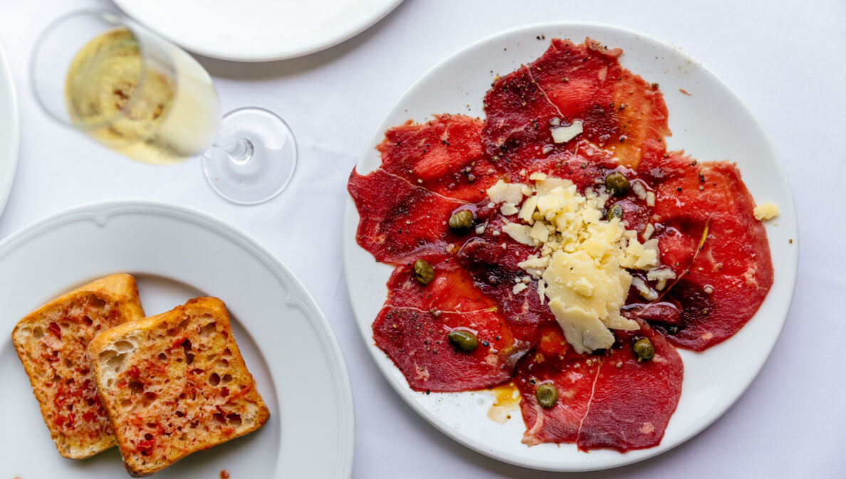 Weiße Teller mit geröstetem Brot und Carpaccio und ein Sektglas