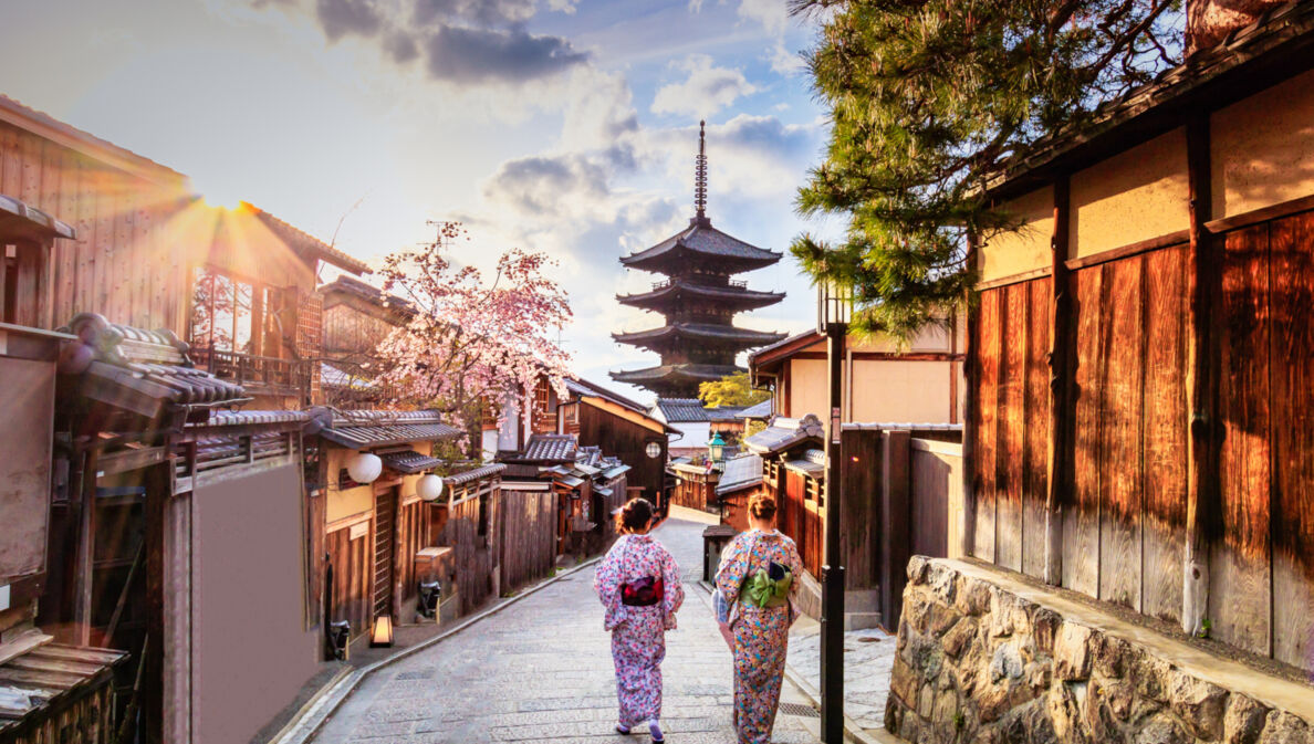 Zwei Frauen in bunten Kimonos laufen durch eine Gasse in der Altstadt von Kyoto auf einen Tempel zu