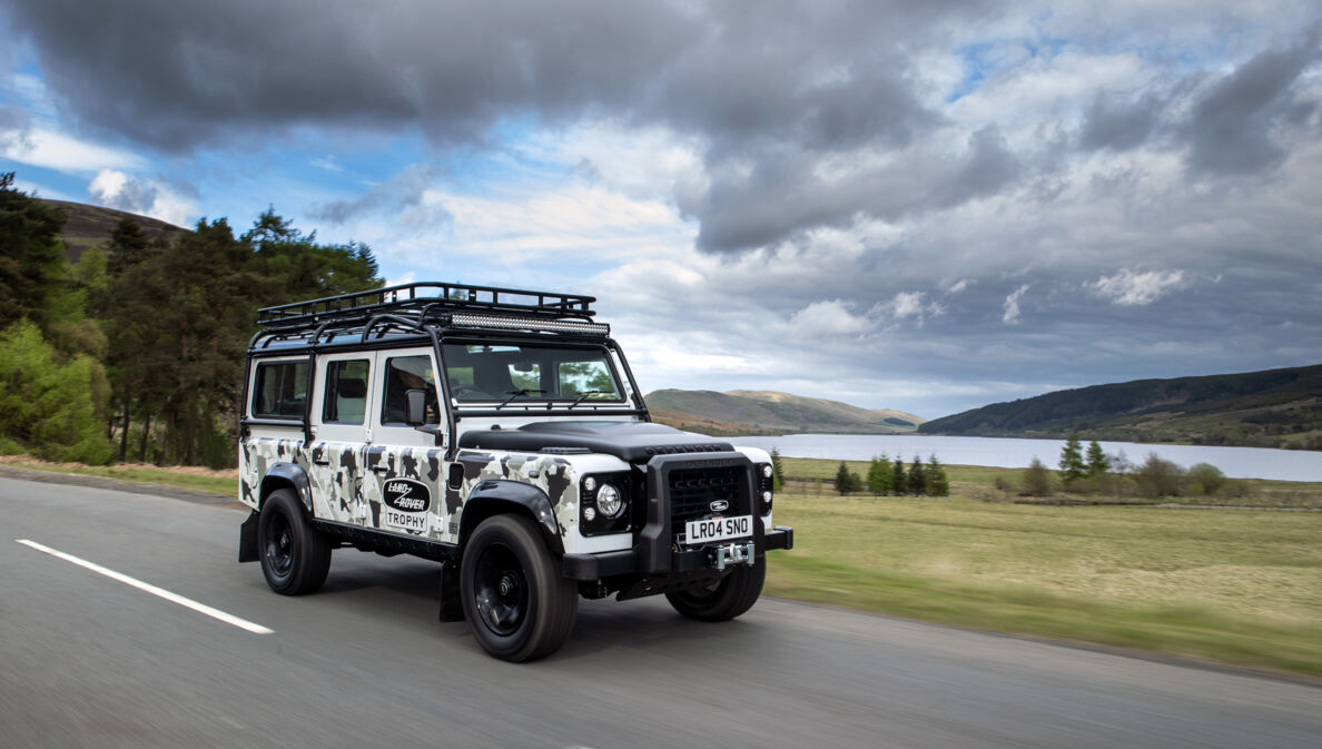 Der Defender Works V8 Trophy II fährt bei bewölktem Wetter an einem See entlang.