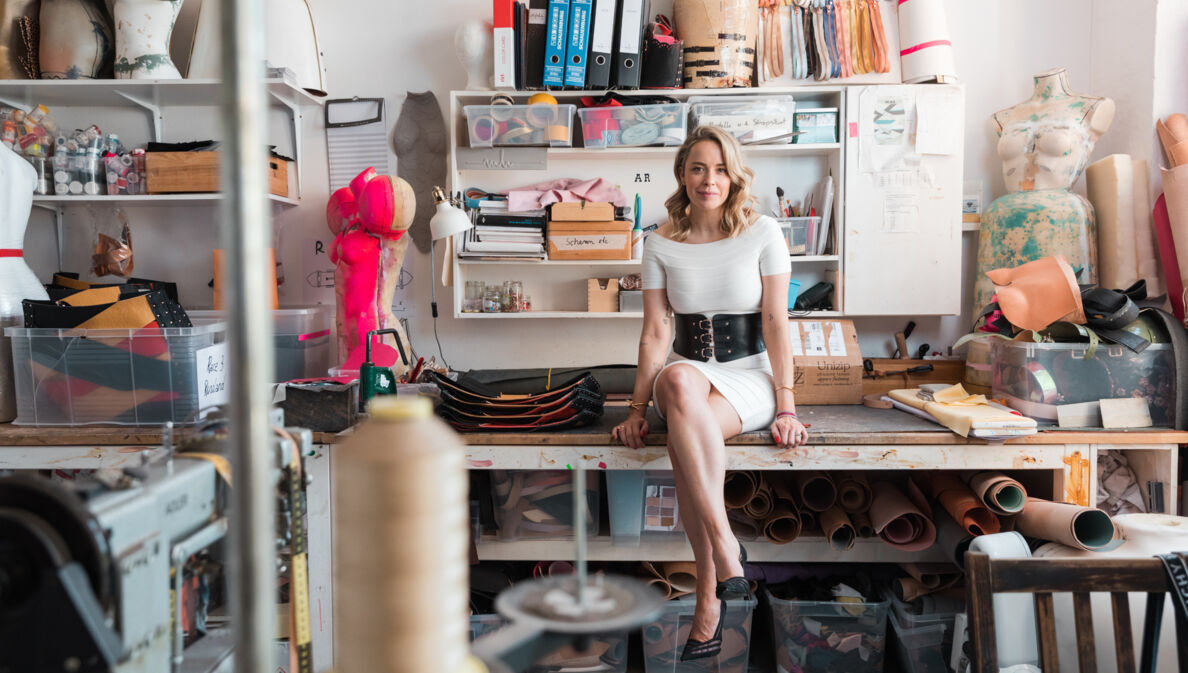 Marina Hoermanseder sitzt in ihrem Atelier auf ihrem Schreibtisch