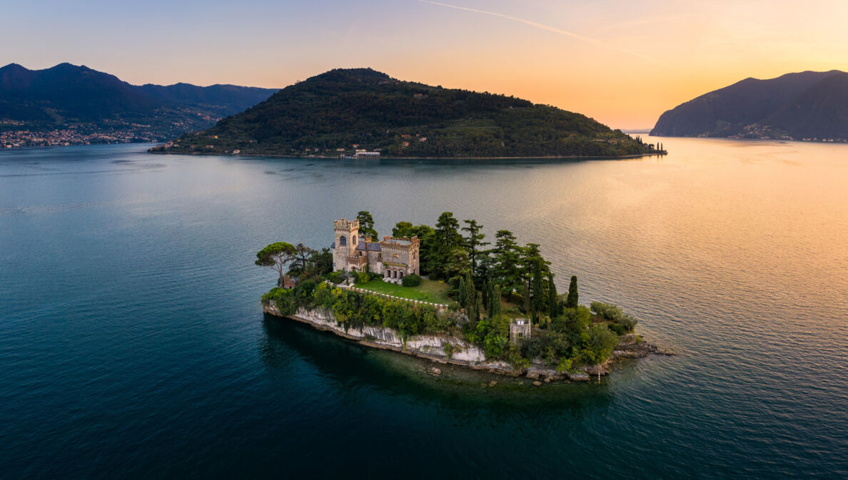 Luftaufnahme einer kleinen Felsinsel mit Burg und Bäumen in einem großen See bei Sonnenuntergang