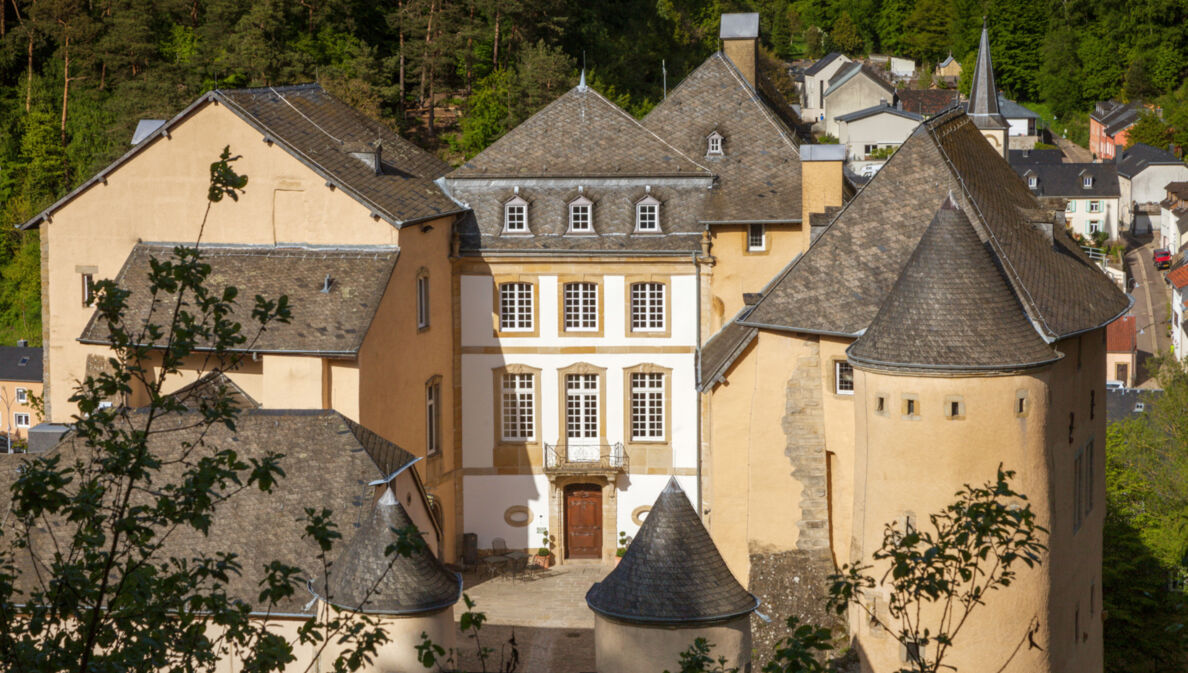 Kleine Burg aus beigem Sandstein mit Rundtürmen und Innenhof in einem bewaldeten Gebiet