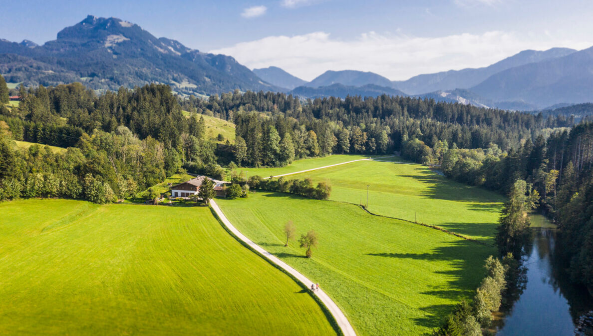 Blick auf eine Landschaft mit Bergen, Wiesen und einem Bach