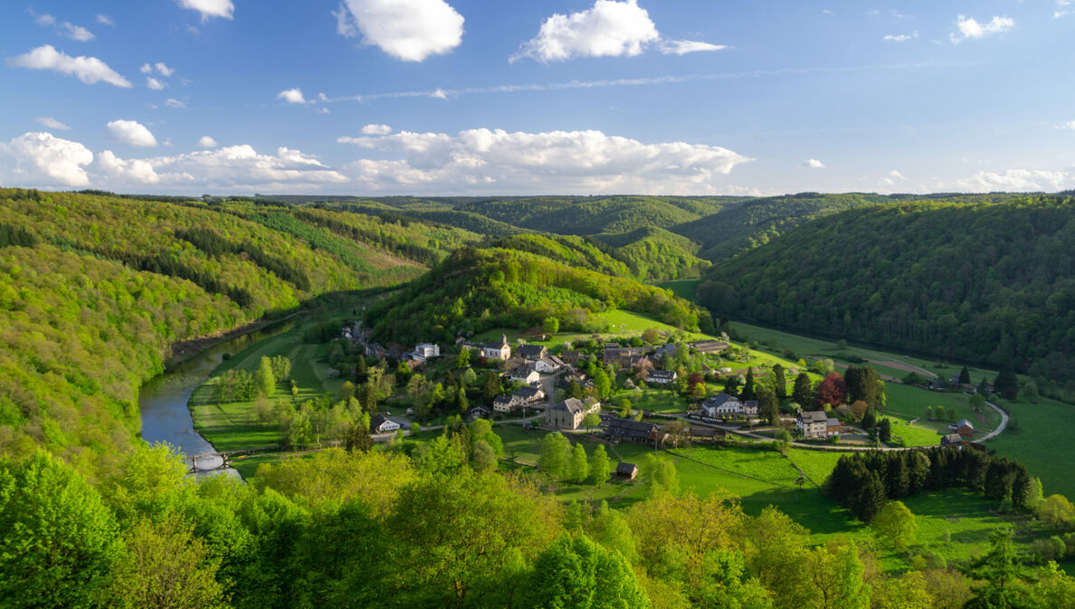 Kleine Ortschaft in einem Flusstal, weitläufig umgeben von hügeliger Waldlandschaft