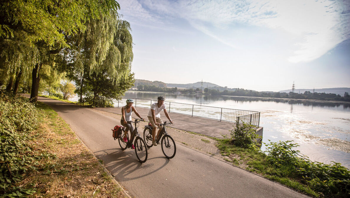 Ein Paar in Sommerkleidung fährt auf Fahrrädern auf einem Radweg entlang eines Flusses