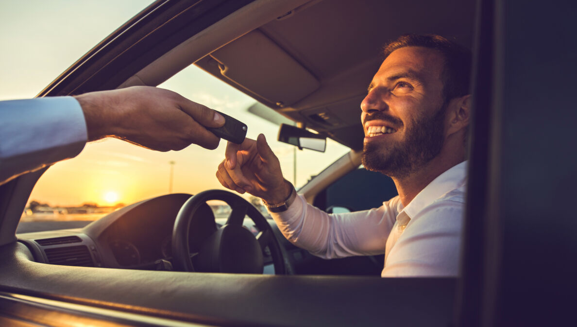 Ein Mann nimmt am Steuer eines Mietwagens den Autoschlüssel durch das geöffnete Fenster entgegen.