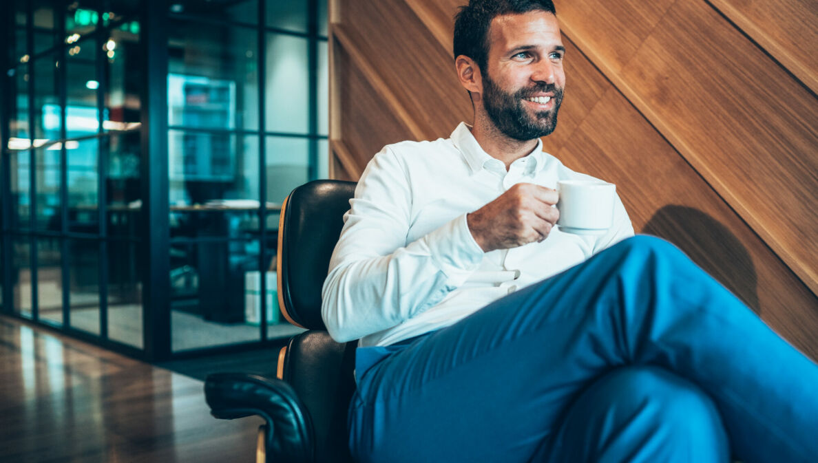 Ein Geschäftsmann sitzt entspannt mit einer Kaffeetasse in einem Sessel in einer Flughafen-Lounge