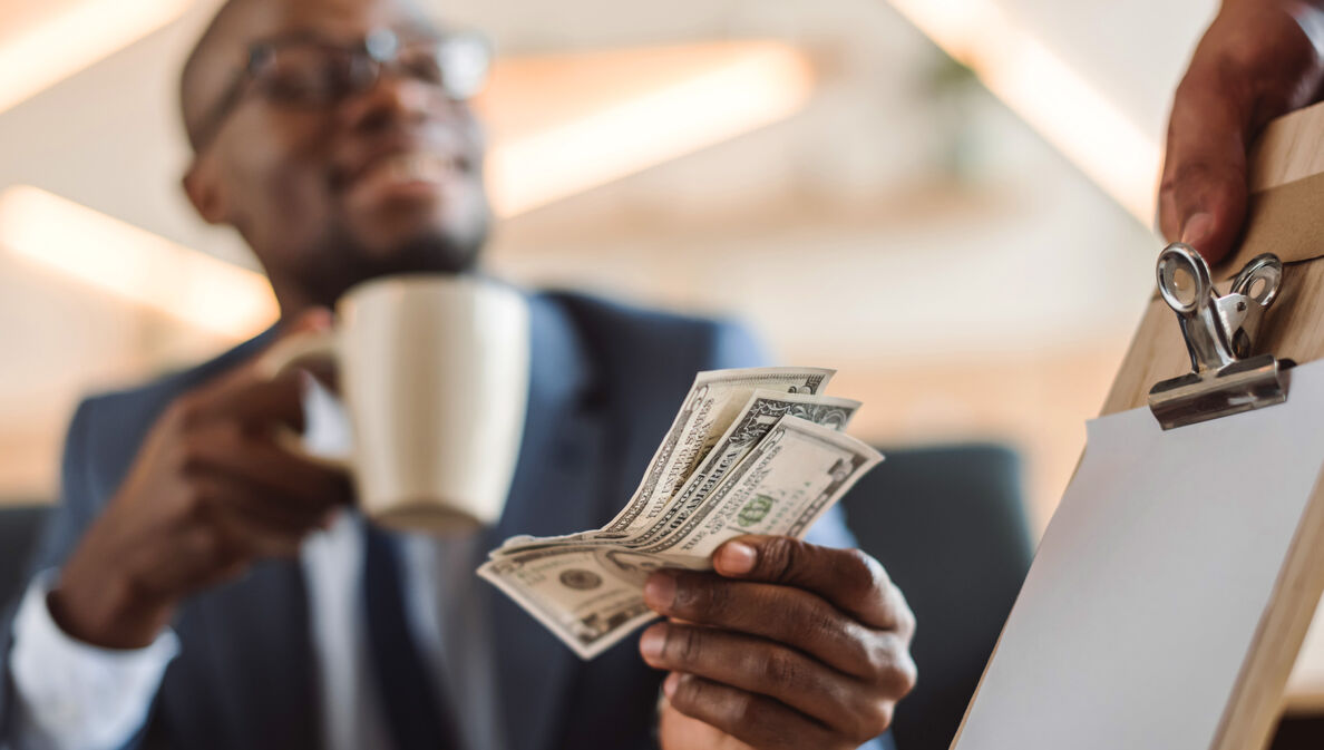 Nahaufnahme von US-Dollar-Scheinen in der Hand eines Geschäftsmannes beim Bezahlen eines Kaffees.