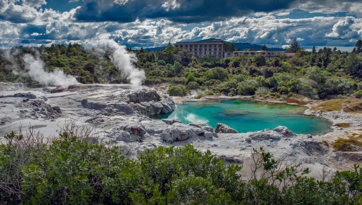 Blick auf Landschaft mit dampfenden Geysiren und grünblauem Wasser