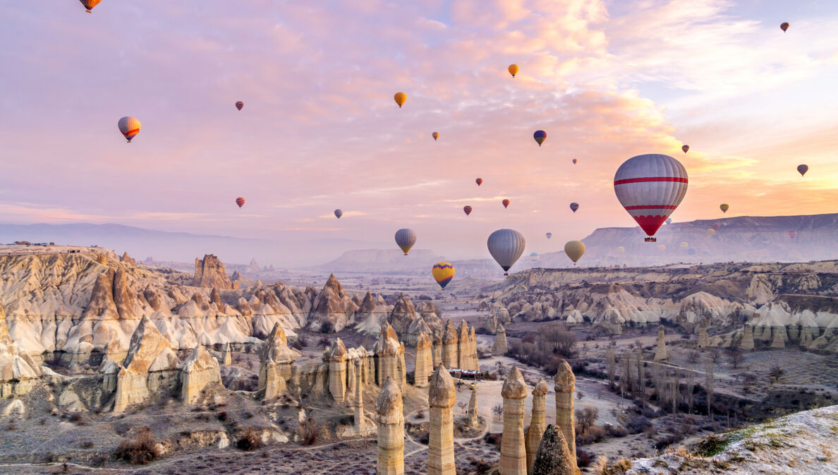 Heißluftballons über einer zerklüfteten Felslandschaft in Kappadokien bei Sonnenuntergang.