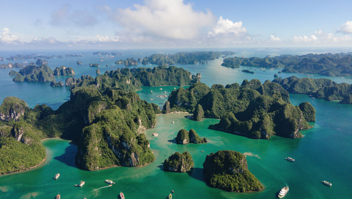 Aufnahme aus der Vogelperspektive von Booten und vielen kleinen von dichter Fauna bewachsenen Inseln in der vietnamesischen Halong-Bucht.