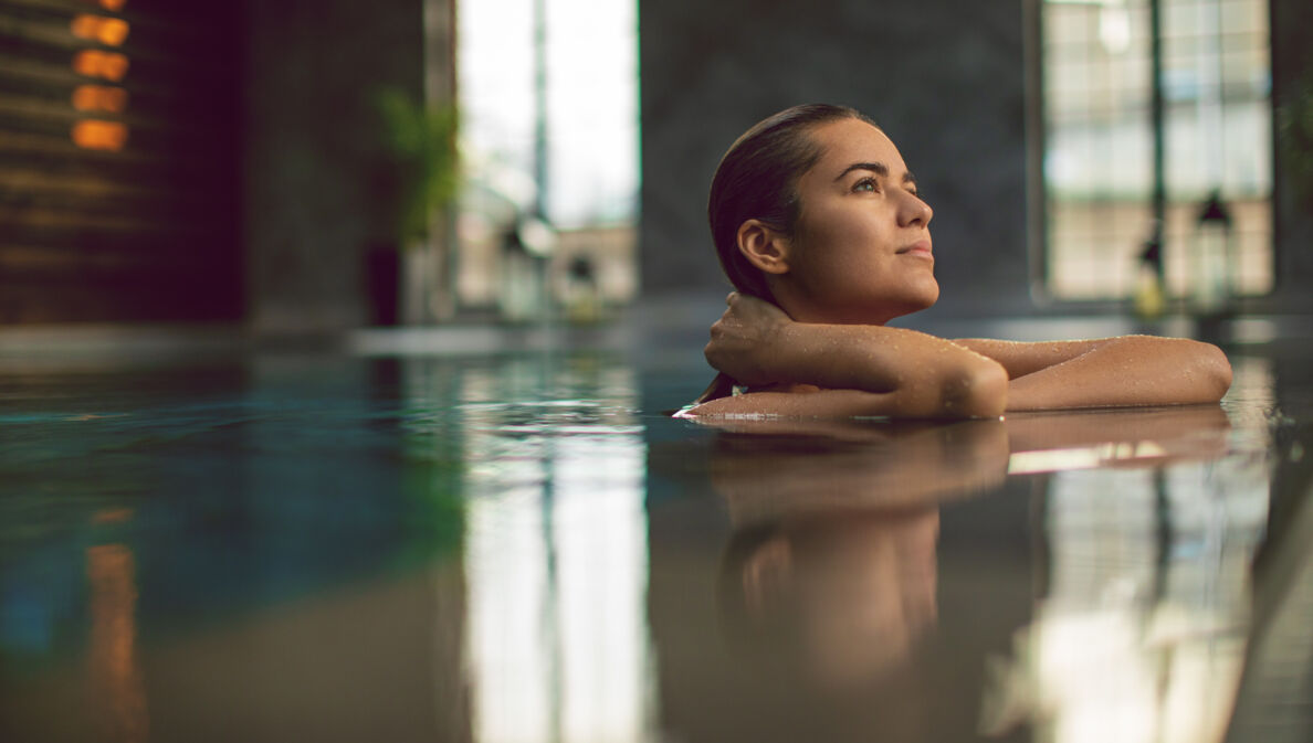 Eine junge Frau entspannt am Beckenrand eines Pools in einem Wellnessbereich.