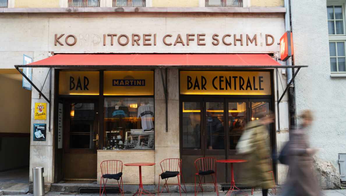 Außenansicht der Bar Centrale mit roter Markise sowie Bistrotischen und Stühlen.