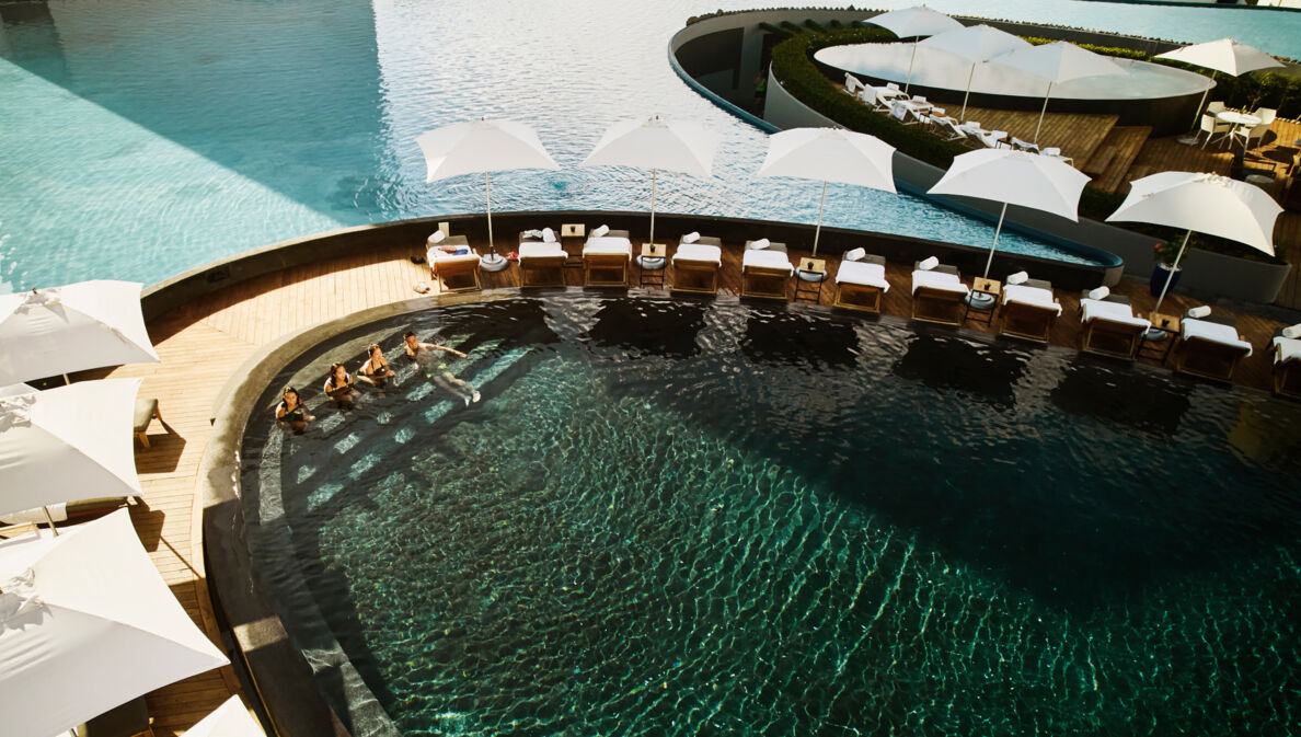 Aufsicht einer modernen Poollandschaft in einer exklusiven Hotelanlage mit Personen im Wasser.