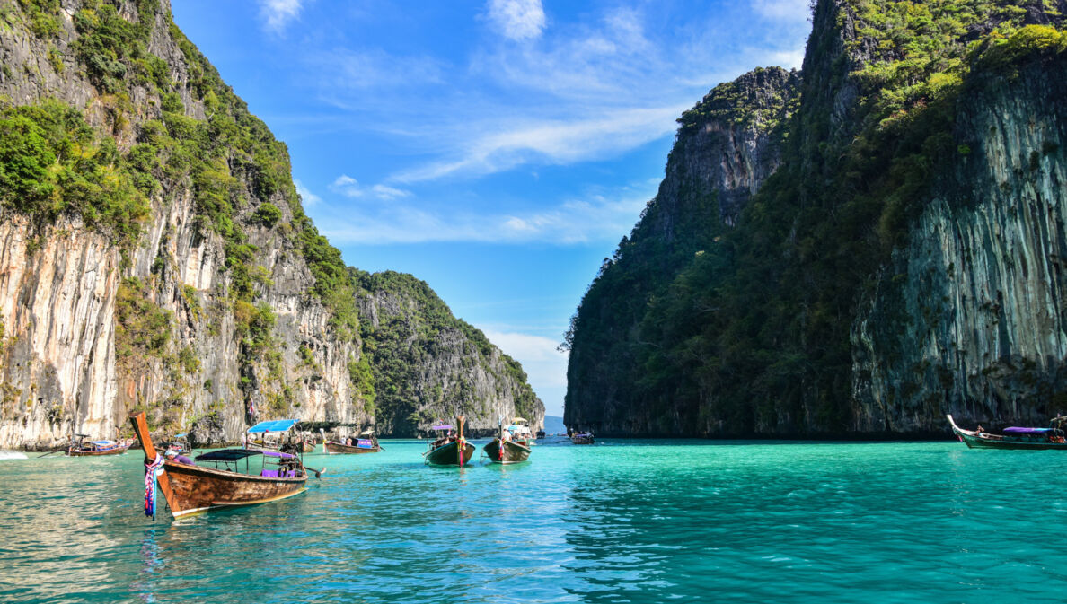 Boote in einer Lagune im türkisblauen Meer mit grün bewachsenen Felsen im Hintergrund. 