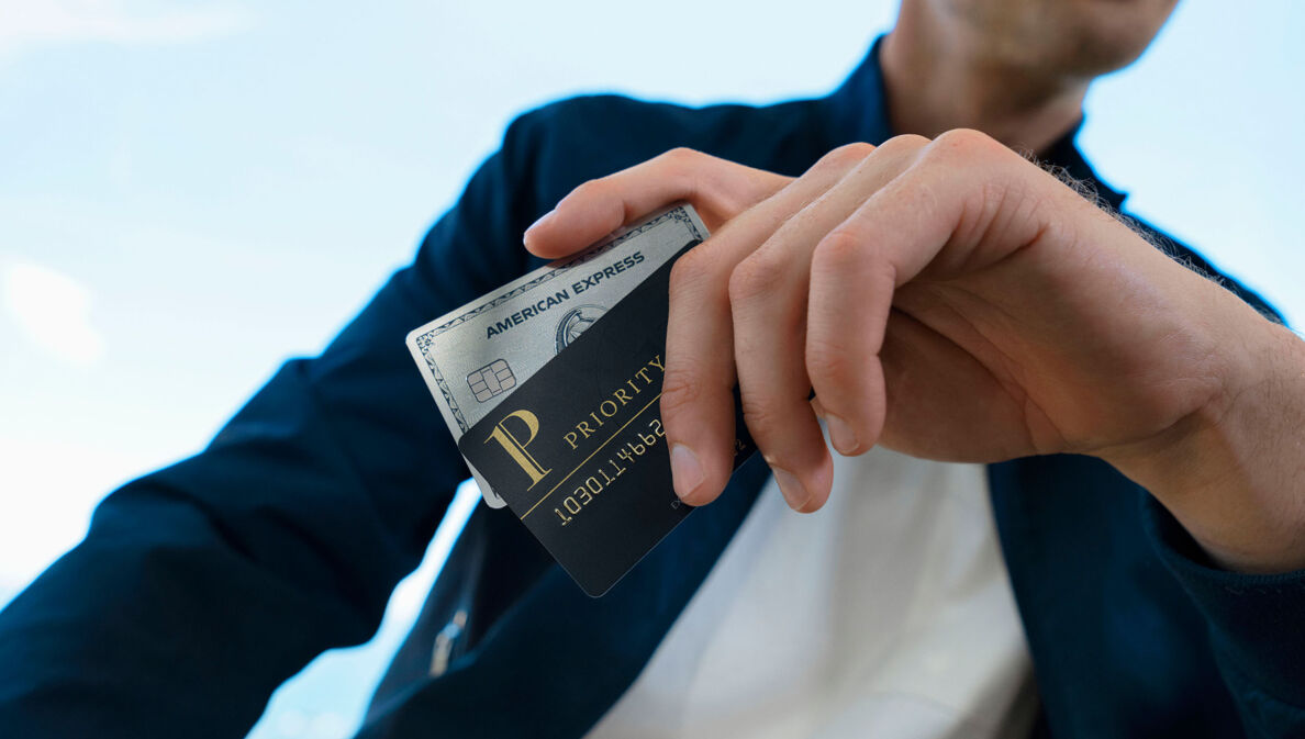 Eine Person hält eine American Express Platinum Kreditkarte mit einer Priority Pass Karte in der Hand.