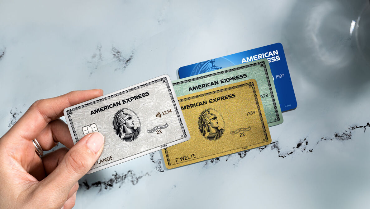 Eine Hand hält eine Platinum Card über eine goldene, grüne und blaue Kreditkarte von American Express.