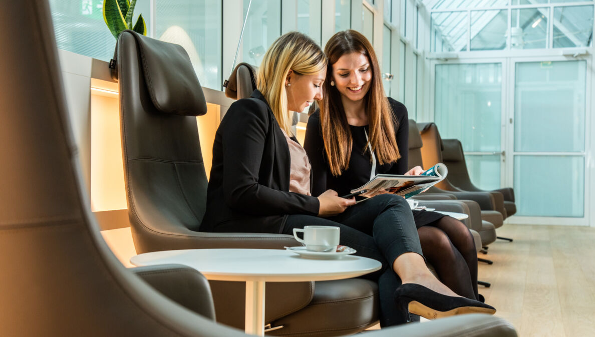 Zwei Frauen auf Ledersesseln schauen gemeinsam auf ein Magazin in einer Lounge.