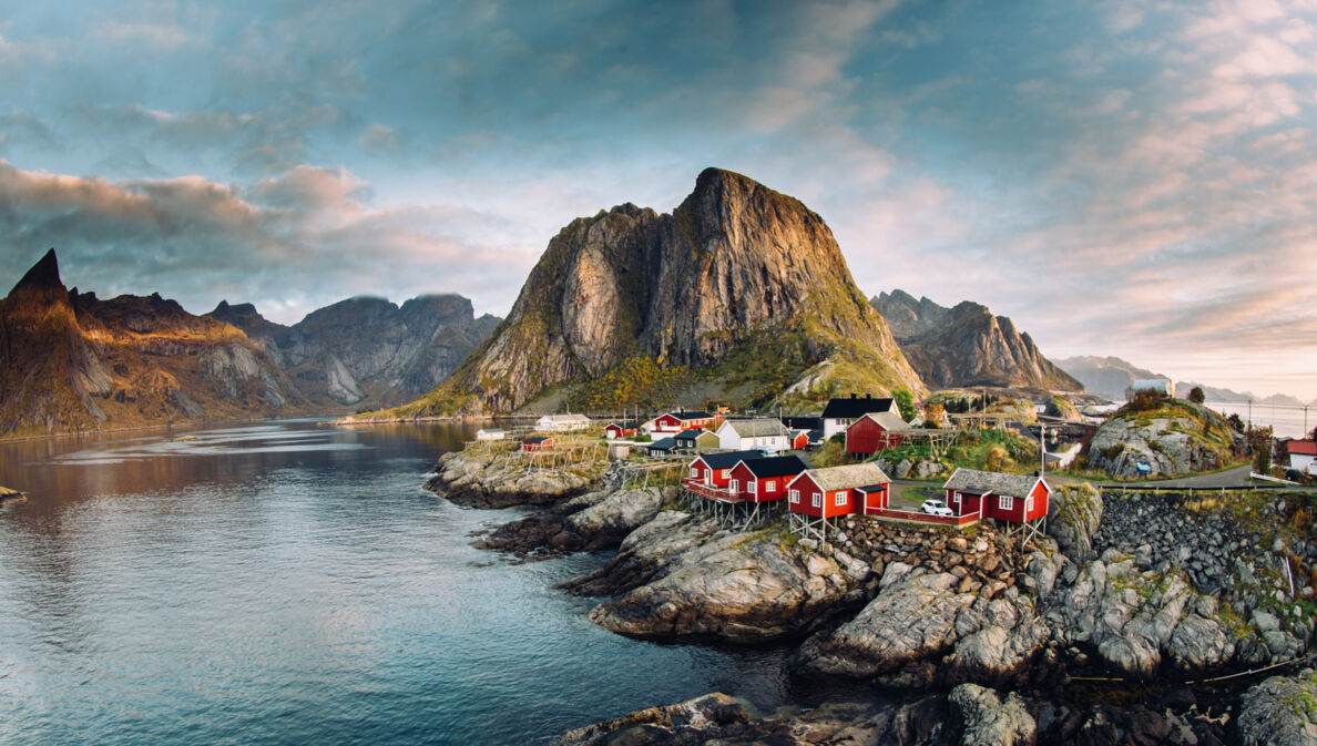 Luftansicht eines Fjords auf den Lofoten mit Felsen, roten Fischerhütten und Bergen.