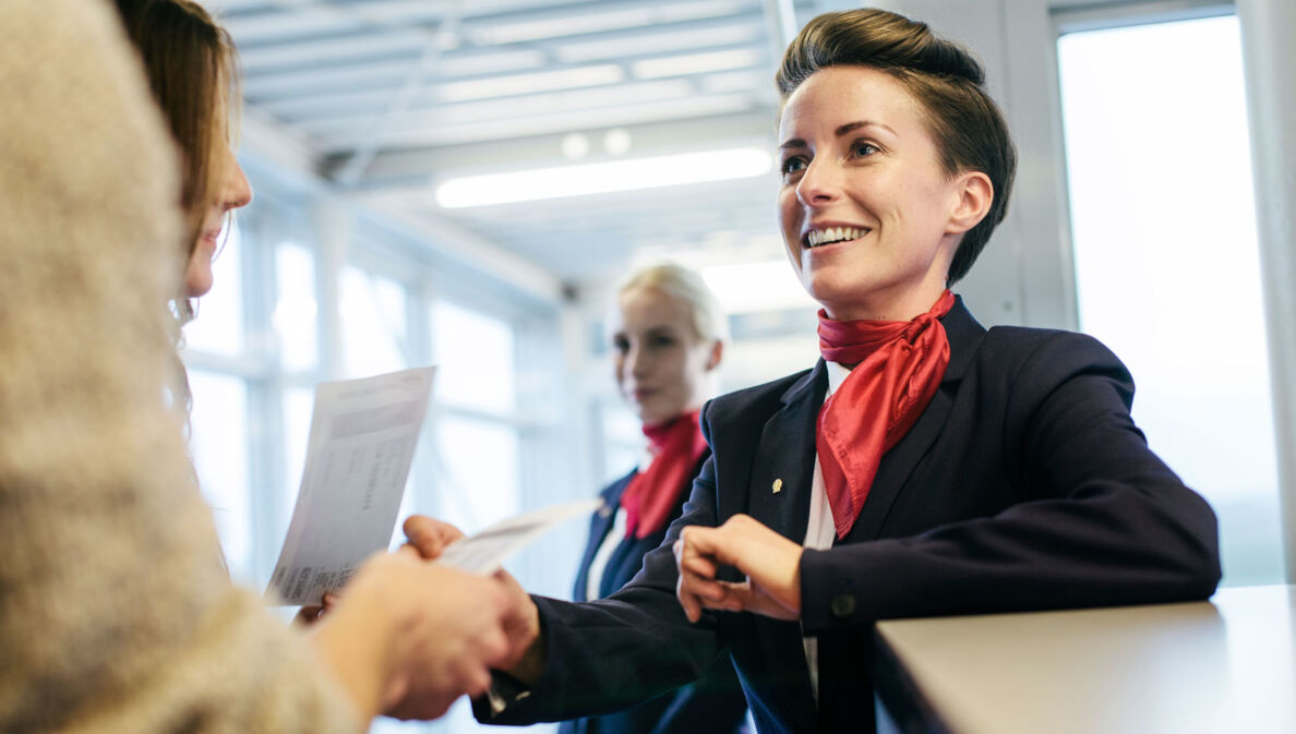 Eine Flugbegleiterin checkt Boardingpässe und begrüßt Reisende am Gate.