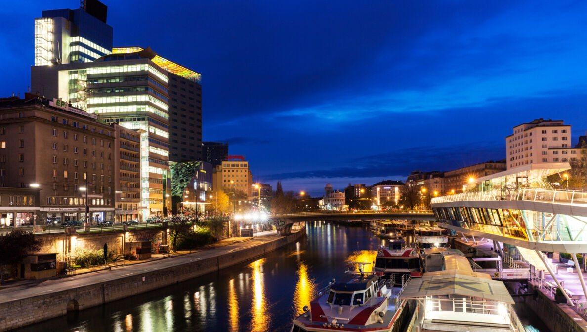 Moderner Hotelkomplex am Donaukanal mit Barkassen in Wien bei Nacht.