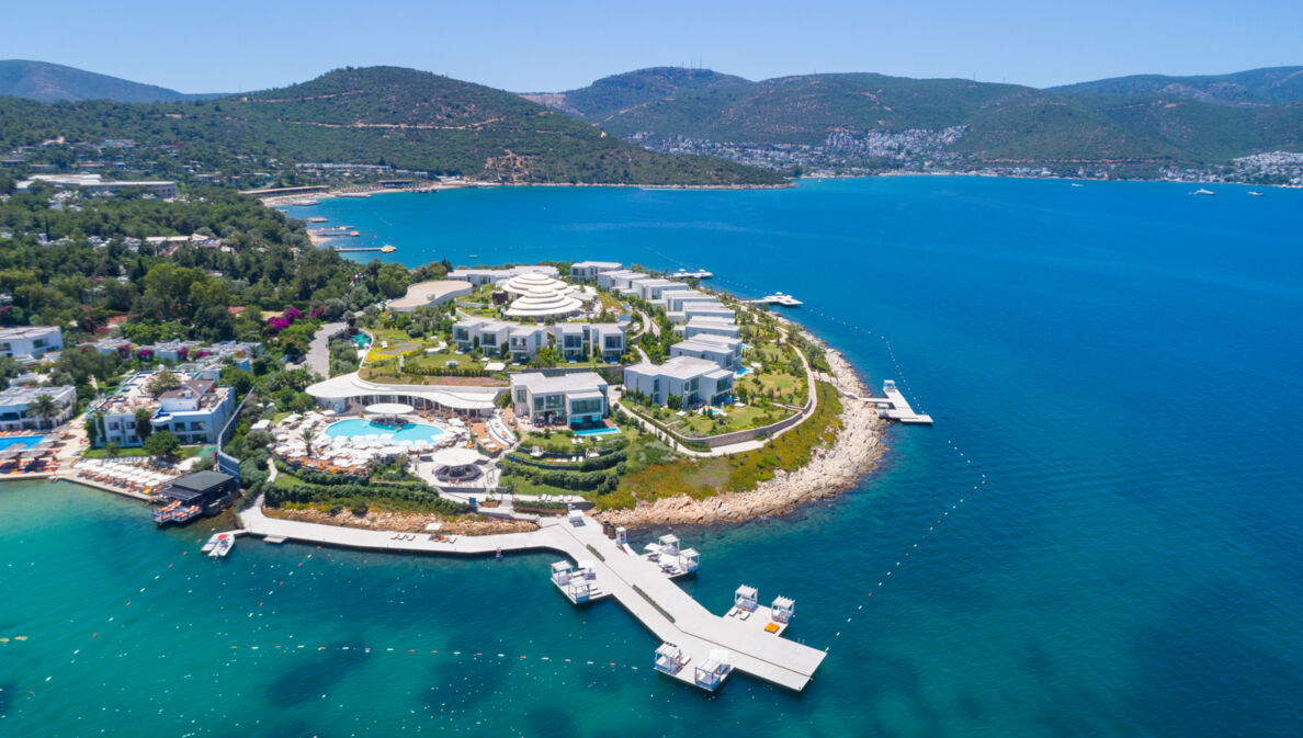 Luftaufnahme eines luxuriösen Hotelresorts mit weißen Bungalows auf einer Landzunge, umgeben von blauem Meer.