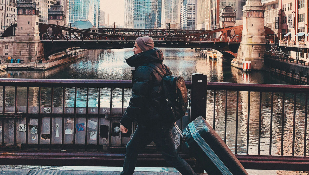 Junger Reisender mit Koffer und Rucksack überquert eine Brücke in Chicago