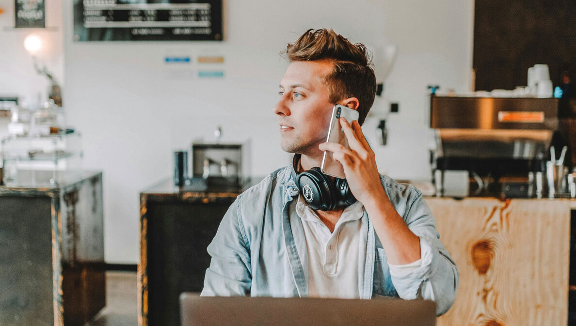 Junger Mann arbeitet im Café am Laptop und telefoniert