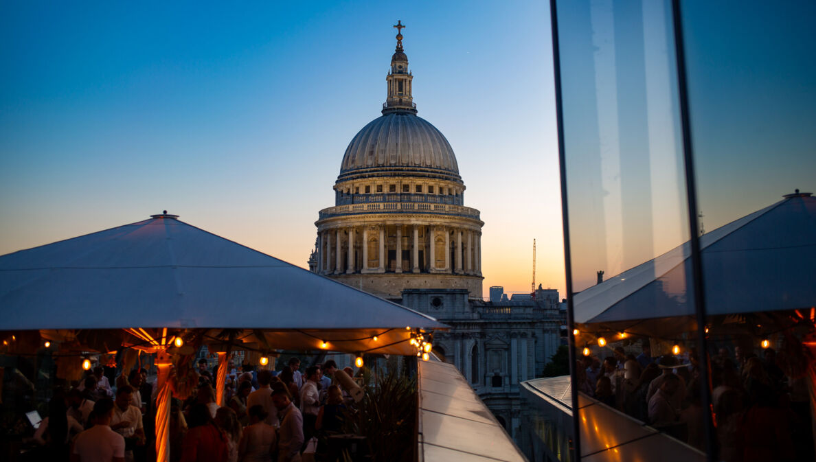 Belebtes Restaurant auf Dachterrasse vor der Kuppel der St Paul’s Kathedrale bei Abenddämmerung.